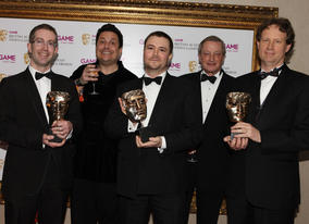 Evan Wells and Christophe Balestra celebrate Empire: Total War's BAFTA in the Strategy category with comedian Dom Joly (BAFTA/Steve Butler).